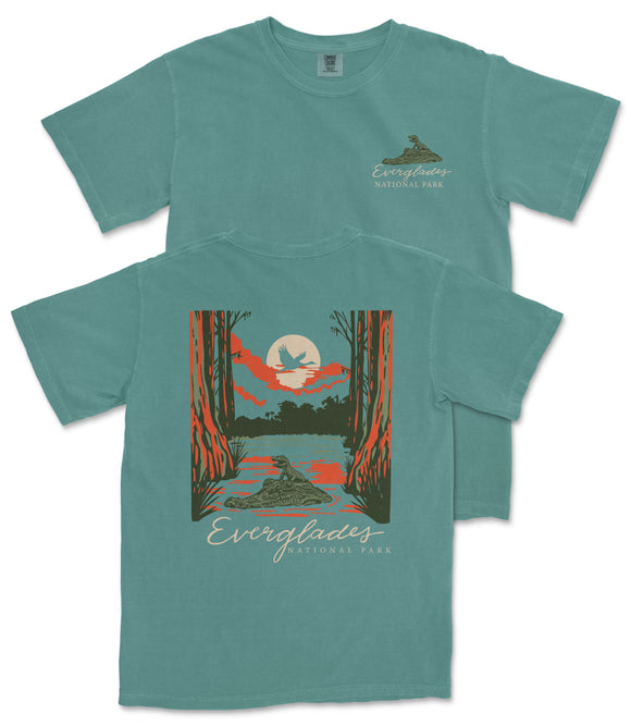 A teal-colored t-shirt with a graphic design depicting a sunset over a lake, surrounded by trees and wildlife.