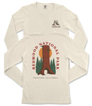 a cream-colored long-sleeved t-shirt with a graphic design depicting a tall tree trunk and a sunset. The design includes the text "REDWOOD NATIONAL PARK" and "NORTHERN CALIFORNIA" printed on the back of the shirt.