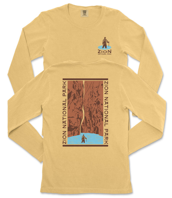 A yellow long-sleeved t-shirt with a graphic design depicting a person standing on a cliff overlooking a body of water, surrounded by mountains.