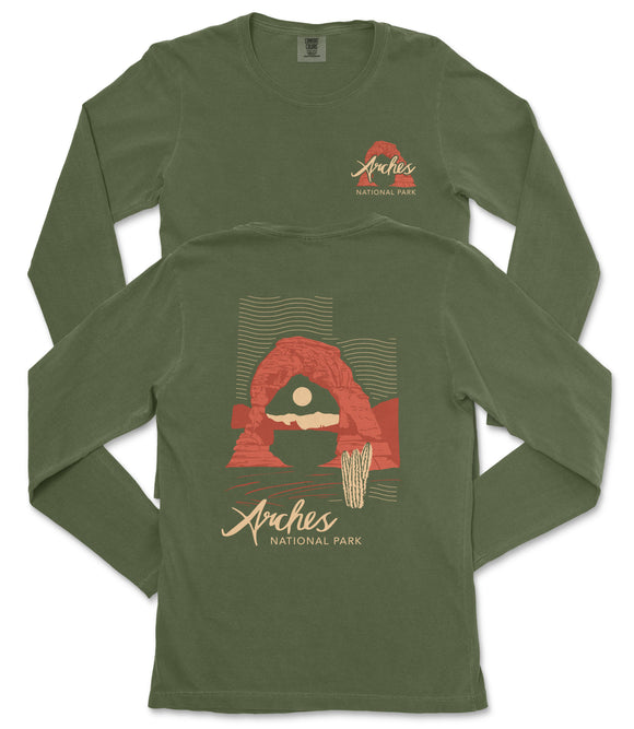 a green long-sleeved t-shirt with a graphic design depicting a desert landscape, including a rock formation and a cactus. The text on the t-shirt reads "Arches National Park".