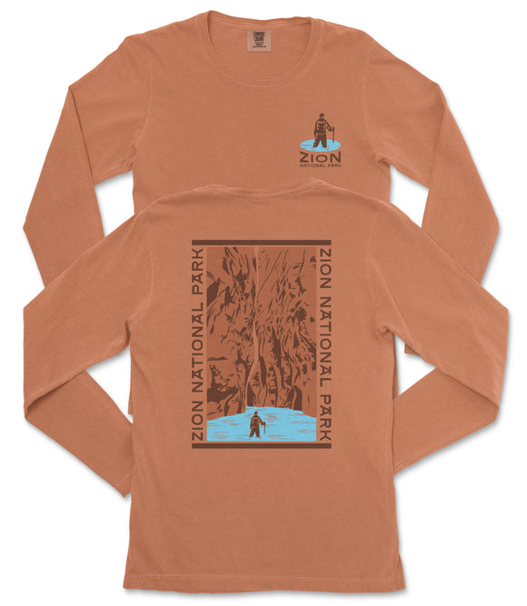 a long-sleeved orange t-shirt with a graphic design on the back, depicting a person standing in front of a waterfall.