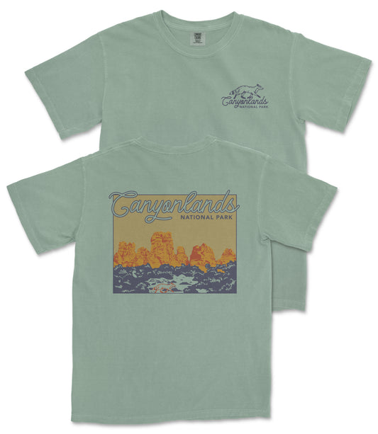 A green t-shirt with a graphic design depicting a scenic landscape with mountains and a river.
