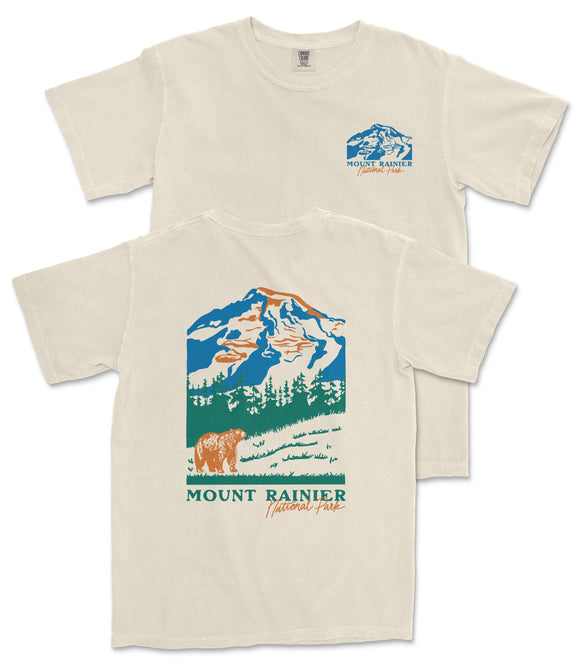 a beige t-shirt with a graphic design depicting a mountain landscape, including a bear and trees. The text on the t-shirt reads "Mount Rainier National Forest" and "National Forest".