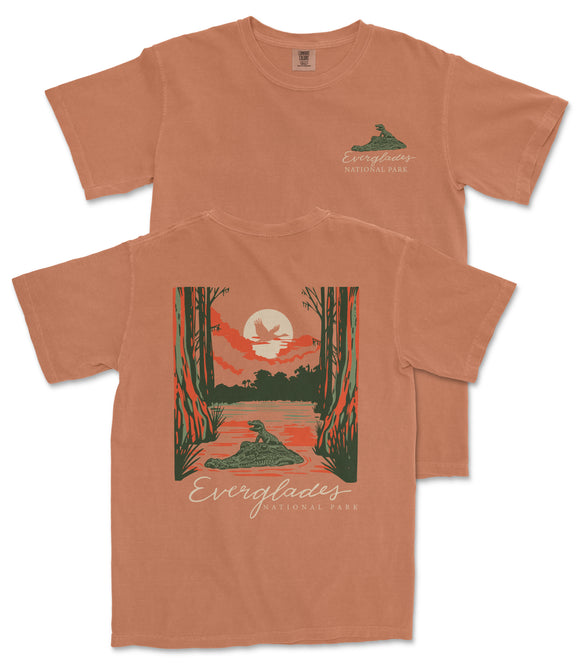 a t-shirt with a graphic design depicting a serene landscape with a lake, trees, and a bird in flight. The text on the t-shirt reads "Everyglades National Park".