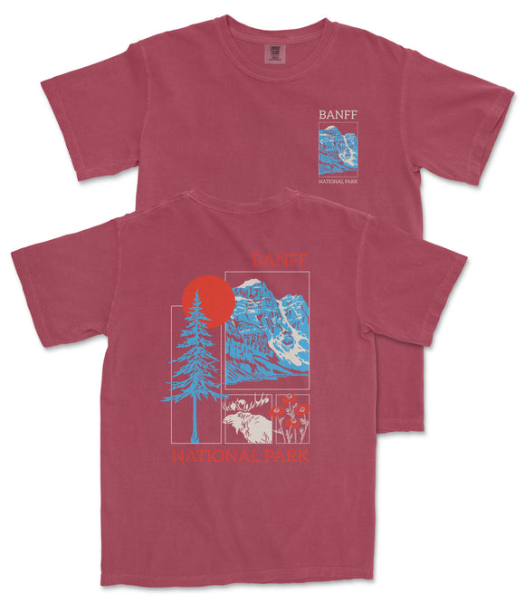 A red t-shirt with a graphic design featuring a mountain landscape, a sun, and various wildlife elements. The text on the t-shirt reads "BANFF NATIONAL PARK".