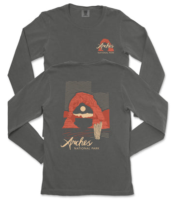 a gray long-sleeved t-shirt with a graphic design depicting a desert landscape, including a rock formation and a cactus. The text on the t-shirt reads "Arches National Park".