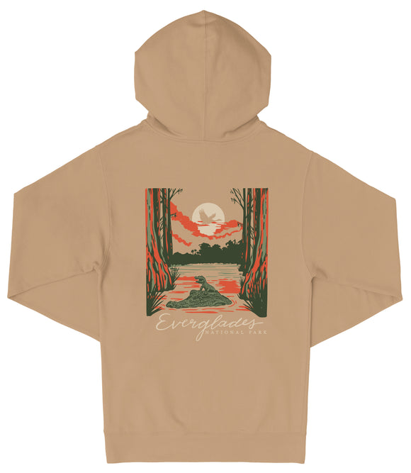 A tan hoodie with a graphic design depicting a sunset over a body of water, surrounded by trees and wildlife.