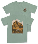 A green t-shirt with a graphic design depicting a mountain landscape and a bighorn sheep, along with the text "Badlands National Park".