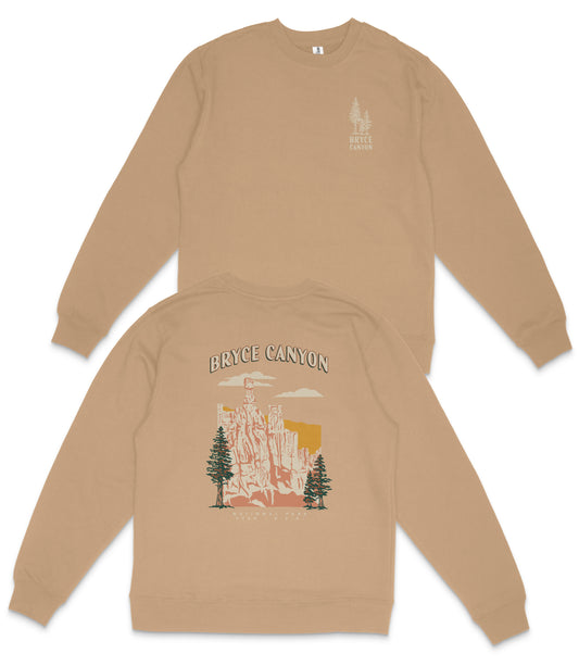 a tan sweatshirt with a graphic design depicting a scenic landscape, including a mountain range and pine trees.