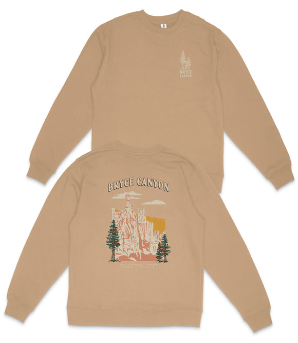 a tan sweatshirt with a graphic design depicting a scenic landscape, including a mountain range and pine trees.