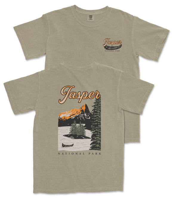 a beige t-shirt with a graphic design depicting a scenic landscape with mountains, a lake, and a canoe. The text on the t-shirt reads "Jasper National Park" and "National Park".