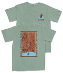 A green t-shirt with a graphic design depicting a person standing in front of a waterfall, surrounded by the text "ZION NATIONAL PARK".