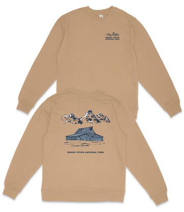 a tan sweatshirt with a graphic design depicting a cabin and mountains, along with the text "GRAND Teton NATIONAL PARK".