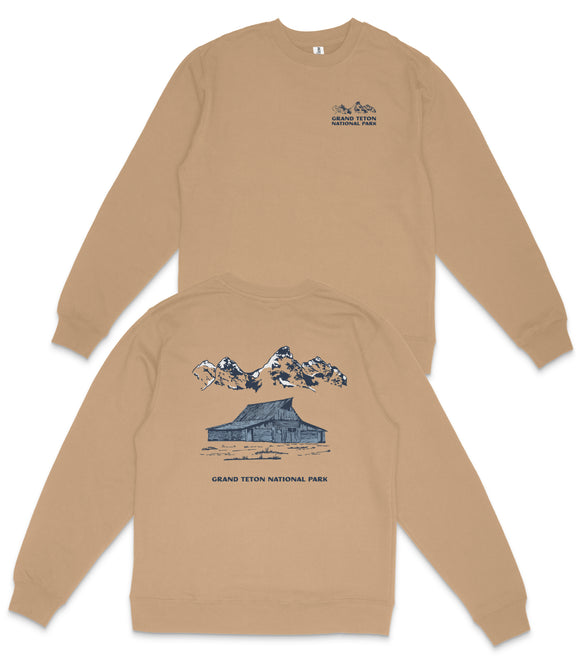 a tan sweatshirt with a graphic design depicting a cabin and mountains, along with the text "GRAND Teton NATIONAL PARK".