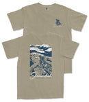 a tan t-shirt with a graphic design depicting a mountain landscape with a person standing on a rock.