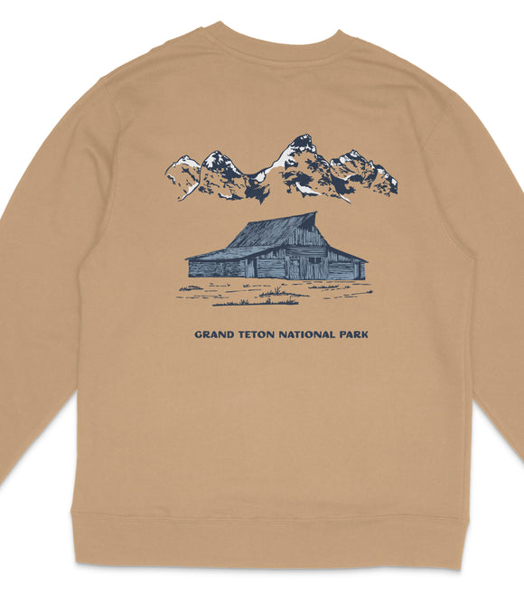 A tan sweatshirt with a graphic design depicting a cabin and mountains in the background, along with the text "GRAND Teton NATIONAL PARK".