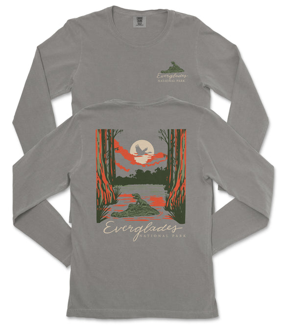 a gray long-sleeved t-shirt with a graphic design depicting a serene landscape with a lake, trees, and a bird in flight. The text on the t-shirt reads "EVERGREENES NATIONAL PARK" and "EVERGREENES".