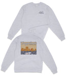 A gray sweatshirt with a graphic design on the back depicting a desert landscape with mountains and a body of water.