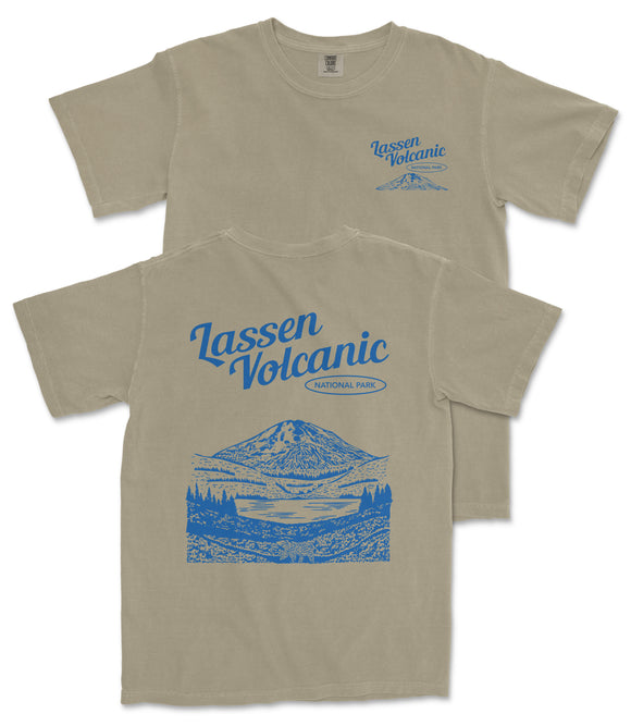 a beige t-shirt with a graphic design depicting a mountain landscape, including a lake and trees. The design also includes the text "Lassen Volcanic National Park" printed on the back of the shirt.