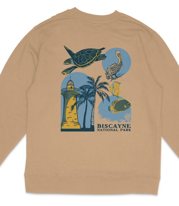 a light brown sweatshirt with a graphic design depicting various elements of the Biscayne National Park, including a lighthouse, palm trees, and marine life.