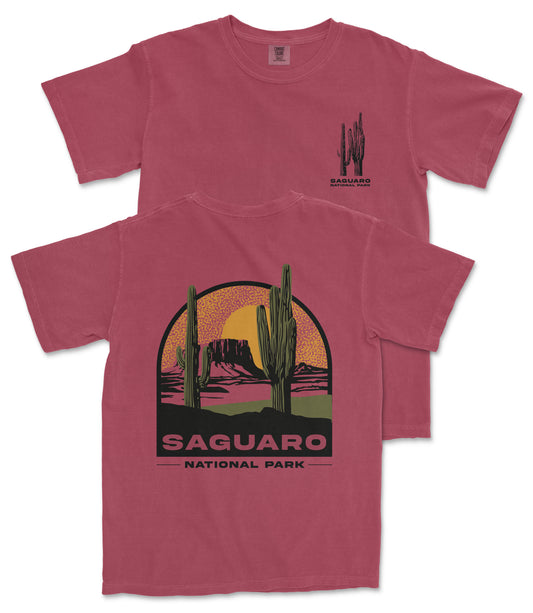 A red t-shirt with a graphic design depicting a desert landscape with cacti and mountains, along with the text "Saguaro National Park".