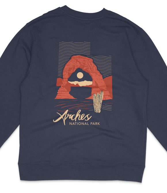 A navy blue sweatshirt with a graphic design depicting a desert landscape with a large rock formation and a cactus. The text "Arches National Park" is printed below the design.