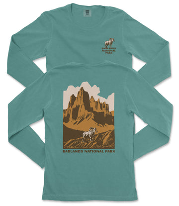 A turquoise long-sleeve t-shirt with a graphic design depicting a mountain landscape and a mountain goat. The text "BADLANDS NATIONAL PARK" is printed on the back of the shirt.