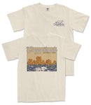 A cream-colored t-shirt with a graphic design depicting a scenic landscape with mountains and water.