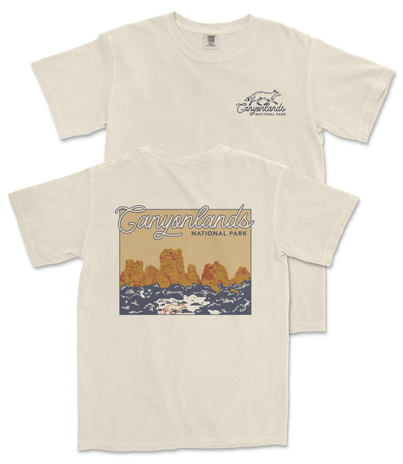 A cream-colored t-shirt with a graphic design depicting a scenic landscape with mountains and water.