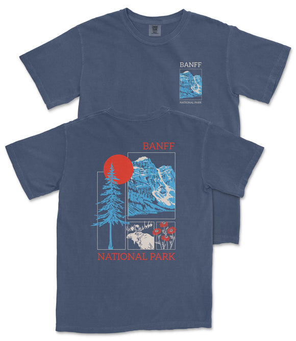 a blue t-shirt with a graphic design depicting a mountain landscape, including a pine tree, a red sun, and various wildlife elements. The text on the t-shirt reads "BANFF NATIONAL PARK" and "BANFF" is prominently displayed in the center of the design.