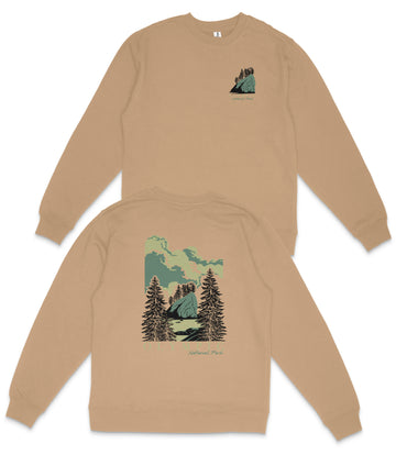 a beige sweatshirt with a graphic design depicting a mountain landscape with pine trees and a cloudy sky.
