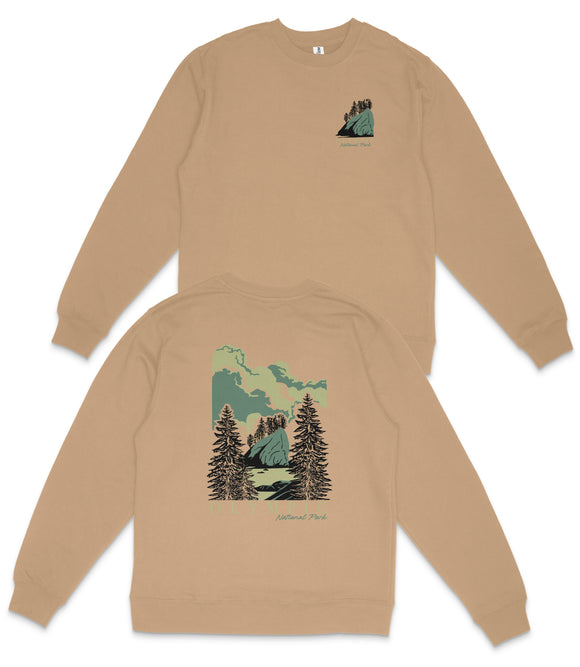a beige sweatshirt with a graphic design depicting a mountain landscape with pine trees and a cloudy sky.