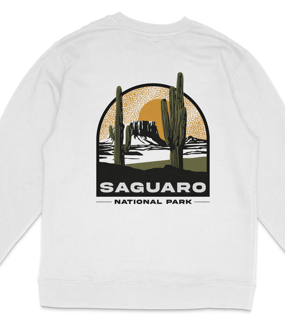 A white long-sleeved shirt with a graphic design depicting a desert landscape with cacti and a sunset in the background, along with the text "Saguaro National Park".