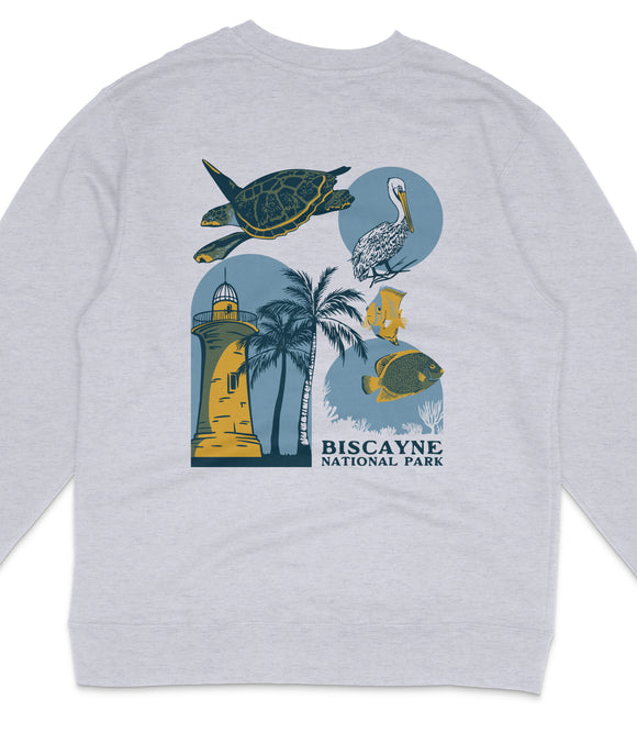 A gray sweatshirt with a graphic design featuring a lighthouse, a turtle, a pelican, and palm trees, along with the text "Biscayne National Park".